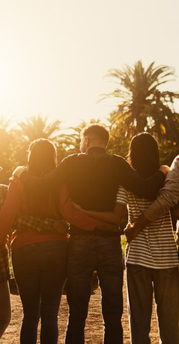 Back view of happy multigenerational people having fun in a public park during sunset time